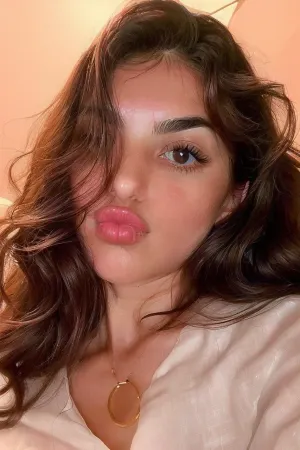 Eine Frau mit langen, dunkelbraunen Haaren und Mandelaugen ist in einer entspannten und ruhigen Pose abgebildet. Ihre Lippen sind in einem weichen Pout geformt und zeigen ihre natürliche Plumpness. Ihre Wangen sind rosig, und ihre Augen