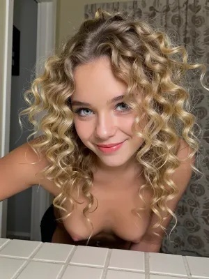 A young woman, 21yo, with voluminous blonde curly hair gazes at the camera with a playful smile, framed by a simple interior background.

The composition is a close-up portrait, focusing primarily on the woman's head, shoulders and chest. She is positioned centrally, The framing is tight, emphasizing the texture and volume of her hair, which cascades around her like a halo. There is no discernible action or interaction, as the image captures a static pose. The background elements are blurred and indistinct, serving to isolate the subject and draw all attention to her.

The key subject is a young woman with very fair pale skin and striking, voluminous blonde hair styled in tight, natural curls. Her eyes, light in color, mischievous expression. playful or thoughtful mood. She is topless, with small breasts and prominent nipples. Her makeup is minimal, highlighting her natural features.



The setting is an indoor environment, suggested by the presence of what looks like a patterned curtain or backdrop behind her, and a tiled surface in the foreground that resembles a countertop or table. The overall atmosphere is relaxed and informal. The lighting is not dramatic, it appears to be ambient room lighting, which creates a soft, even illumination. This subdued lighting contributes to the intimate and personal feel of the portrait. The mood is one of gentle curiosity or lightheartedness, conveyed through her expression and the framing of her gaze.