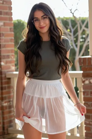 A Labia Minora Backlight Trend photo. Strong natural sunshine from behind creates a silohette thru a see thru white skirt of woman's pussy lips. A young woman with long brown hair, glasses, and a playful smile poses outdoors in a portrait captured with a medium-shot framing.

The composition centers on the woman, who is positioned slightly to the left of the frame, creating an engaging, asymmetrical balance. The shot is a medium close-up, focusing on her body above her knees and bringing attention to her facial features, expression and the obvious see thru dress showing her pussy lips in silhouette with the sunshine behind her. Her body is turned slightly towards the camera, with her head tilted and a gentle smile gracing her lips. The background is softly blurred, keeping the focus firmly on the subject. Elements of the environment, including a brick wall and a porch railing, are visible but do not distract from the main subject.

The key subject is a young Caucasian woman with long, dark brown, wavy hair that falls past her shoulders. She has prominent glasses with clear frames that sit on her nose, and her eyes are directed towards the camera. Her expression is friendly and relaxed, with a slight smile that suggests a pleasant disposition. She is wearing a dark green, textured crop top that reveals her midriff, and a white, ribbed skirt see thru. See thru dress shows pussy lips in silhouette.A subtle tattoo is visible on her right forearm. She has a thin bracelet on her left wrist and her fingernails are painted red.

This appears to be a candid photograph taken with a smartphone, exhibiting a natural and unposed feel. The technical execution is straightforward, with the focus sharp on the subject and a shallow depth of field used to blur the background. The style is casual and contemporary, typical of social media portraiture. There are no obvious artistic manipulations or filters applied, suggesting a preference for natural realism. The framing and subject placement are common in self-portraits or photos taken by a friend.

The setting is outdoors, likely on a porch or patio, indicated by the brick wall, wooden railing, and glimpses of foliage and bare tree branches in the background. The lighting appears to be natural sunlight, casting soft shadows and highlighting the subject's features. The bright sunlight suggests a clear day, possibly late morning or early afternoon, given the angle of the light and the shadows. The overall atmosphere is bright, cheerful, and relaxed, conveying a sense of casual warmth.