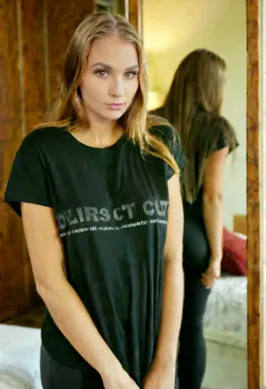 exact woman from the reference photo, identical face, standing in front of a large mirror, looking at her own reflection, oversized dark t-shirt, bedroom, soft lighting.