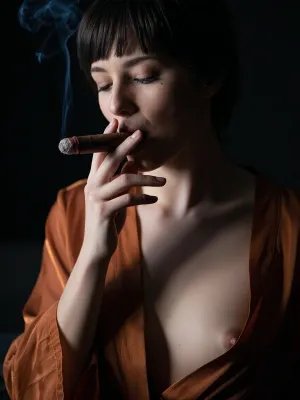 close-up portrait of Katie, barely visible in the darkness, the light catches the cigar held loosely between her fingers, smoke rise from the cigar, the end of the cigar glows faintly, utterly self-possessed., (Katie is a 20ish woman, dark orange transparent silk dressing gown open, short dark hair with fringe, her skin is pale and almost white, tiny breasts and nipples), eyes closed or half open, expression languid and satisfied. Total darkness, smoky, deep shadow, heavy grain, warm and cinematic, single defused backlight, faintly illuminated with a faint hint of blue the haze, the haze is more visible than the figure, the figure dissolved and softened by the smoke. The background is dark with no visible detail.