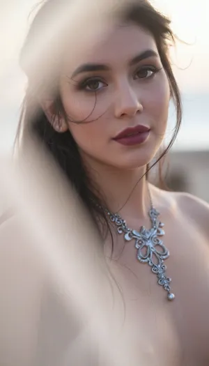 A vertical cinematic closeup portrait with an ethereal, soft-focus aesthetic, defined by diffused light. The subject is an enigmatic young Latina woman with long dark hair and wispy strands that have a soft luminous halo framing her elegant facial features with stray strands of windblown hair. She wears dark smoky makeup that highlights her large expressive eyes, while her soft full lips are a deep matte berry. Her elegant neckline is accented by an intricate antique silver gothic necklace. The soft lighting and shadows flatter her slender body. The scene is enveloped in a powerful but diffused golden-hour glow from the side, which creates a luminous light bloom on her skin and the fabric, dissolving sharp edges in an ethereal haze. The background is a very blurred, dreamlike pastoral pastel lavender-gray coastal sky, soft and bright. The overall mood is serene contentment. Shallow depth of field, subtle film grain. This is a high-key photograph.