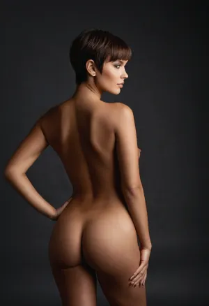 A stunningly gorgeous, fully naked woman standing in a seductive, randomized pose that exudes confidence and allure. Her body is a flawless masterpiece of feminine curves, with her full breasts and round hips drawing the eye, and a tight, toned stomach that suggests she takes care of herself. Her eyes, a vibrant dark chocolate brown, sparkle with a playful mischief that hints at secrets untold. Her hair, very short brown pixie hair with bangs, frames her face and emphasizes her high cheekbones. The absence of any background, setting, props, or mood allows her beauty to be the sole focus, leaving the viewer to imagine the infinite possibilities of her story. She stands with a slight arch in her back, one hand resting on her hip, and the other playing with the strands of her hair, as if she knows she's being admired and is enjoying the moment. Her skin is a canvas of perfection, unmarred by any imperfections, and it seems to glow under the unseen light source. Her posture and expression are open, inviting the viewer to appreciate every inch of her amazing form. The lack of clothing leaves nothing to the imagination, showcasing the artful randomness of nature's palette in her body's design. This image is a celebration of the female form, stripped of all but the essentials, beauty, confidence.