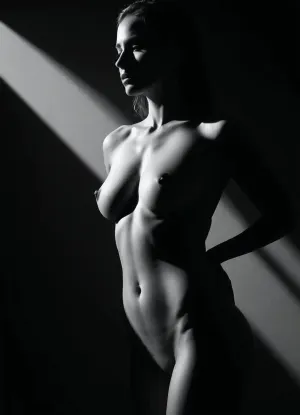 Cinematic black and white studio photography, sexy sculpted obliques highlighted by dramatic rim light, shaped belly, strong shadows carving the waistline, minimalist photography studio, fine art nude-inspired aesthetic, powerful yet sensual mood, vertical composition, upturned nose, looking straight to the viewer, deep and intense gaze