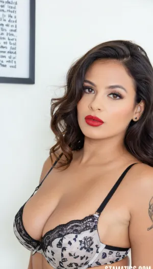 High-end editorial portrait photography of an adult Indian woman, accurately matching the subject’s physical appearance and proportions. Medium close-up framing from upper chest to head, preserving realistic facial structure, eye shape, nose, lips, and jawline. Curvy, full-bodied physique with accentuated bust and soft natural contours.

Naked. A chest tattoo in elegant cursive script clearly reads “Simone”, positioned above the bust and fully legible, treated as a key identifying visual element.

Warm brown skin tone with natural texture, subtle highlights. Dark black wavy hair with volume, side-parted, falling naturally over the shoulders. Bold red lipstick, defined eyes, minimal but polished editorial makeup. Expressive gaze directed slightly upward and off-camera, calm and confident expression.

Soft, diffused studio lighting, neutral background, controlled contrast to preserve realism. Accurate anatomy, correct proportions, no stylization or exaggeration. Shallow depth of field, sharp focus on face, lingerie fabric, and tattoo text. Clean editorial composition, magazine-quality realism, cinematic photographic style, high resolution.