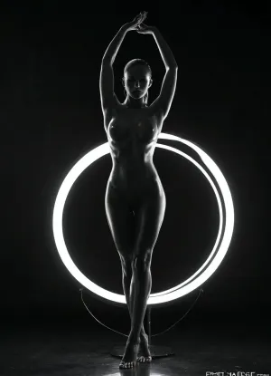 The scene features a striking figure posed elegantly against a deep black backdrop, highlighting the interplay between light and shadow. Central to the composition are two large circular light rings, glowing bright white, which create an arresting visual contrast against the darkness. The figure, whose outline is softly illuminated by the lights, stands sensually within the rings, with arms raised and hands gently gripping the edges, adding to the dynamic nature of the pose. The lighting emanates from the rings, casting subtle shadows that sculpt the contours of the body, emphasizing its form and curves in a way that draws the viewer's eye to the graceful lines. The overall ambiance is both dramatic and intimate, enhanced by the smoky atmosphere that subtly obscures parts of the background and adds depth to the scene. The color palette is monochromatic, dominated by shades of black and white, creating a timeless and elegant aesthetic. This carefully crafted composition, with its bold use of light and shadow, invites the viewer to appreciate the beauty of the human form within a modern, artistic context., ultra detailed, intricate details, cinematic, photorealistic, masterpiece