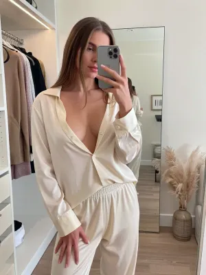 A masterpiece, top-notch quality, ultra-high detail, a realistic lifestyle-style photo in the mirror, (selfie), . A candid shot with soft, natural morning light. Composition, a realistic full-length selfie featuring an incredibly attractive Instagram model. She stands directly in front of a huge, minimalist floor-to-ceiling mirror in her stylish and luxurious walk-in closet, holding a smartphone to take a photo of her outfit for her “Stories.” The girl has tilted her head slightly, looking at the phone screen in the reflection with a soft, confident half-smile. The smartphone rests elegantly in her right hand, partially obscuring the center of her face, her hand is rendered with anatomically flawless detail, five clearly defined, slender fingers and a neat, natural manicure. Outfit and skin, She is wearing a premium, loose-fitting silk loungewear set in creamy pastel tones, consisting of a partially unbuttoned silk blouse and wide-leg pants. The unbuttoned collar elegantly reveals the upper part of her chest, her graceful collarbones, and her smooth neck. Background in the reflection, The mirror reveals a bright, tidy, minimalist-style walk-in closet with open clothing shelves, warm, stylish lighting, and a bouquet of pampas grass in a ceramic vase in the corner. Soft bokeh, authentic social media aesthetics, high resolution