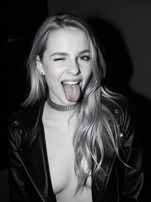 raw photo, A high-contrast black-and-white portrait captures a young woman in her twenties framed in a medium close-up shot from an eye-level perspective. She faces directly toward the camera with an animated, playful expression, winking one eye while sticking her tongue straight out. Her long, blonde hair is styled with soft waves and parted slightly off-center, flowing down over her shoulders. She has a slender build with a moderate chest visible beneath her attire. She wears an open black leather jacket over a low-cut dark top. A thick, metallic choker necklace sits at the base of her neck, accompanied by small hoop earrings visible near her jawline. The direct frontal flash creates sharp highlights on her face, collarbone, and the sheen of her leather jacket, casting deep shadows in the background. The background remains dark and largely uncluttered, drawing full focus to the subject. The monochromatic tonal range emphasizes bright highlights against rich, dark tones, giving the image a grainy, classic analog aesthetic reminiscent of candid flash photography.