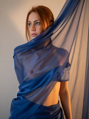 A woman standing against a wall, wrapped in a translucent blue-blue, flowing cloth. The woman has redhead hair and looks thoughtful, deep green eyes, and the fabric reveals a part of her body, creating spectacular and intriguing lighting. The decor seems minimalistic, with a warm, golden light that highlights the drapery of the fabric and the figure of the model. The focus is on the interaction of the figure and the fluttering fabric.