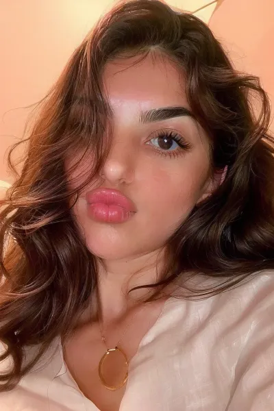 Una donna con capelli lunghi e scuri e occhi a forma di mandorla è raffigurata in una posa rilassata e serena. Le sue labbra si formano in una morbida ciambella, mostrando la sua naturale prugna. Le sue guance sono rosee e i suoi occhi