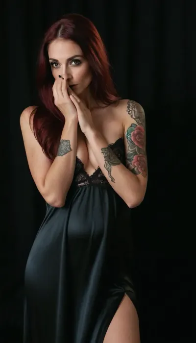 Skinny 25 years woman, long straight dark red hair, Tall, slender woman, black eyebrows, black eye shadow, Absolute darkness around, black background, photostudio, photorealistic, stunning quality, 4k, very large tits, bjg ass, ((black satin nightgown with lace)), (one arm tattooed from shoulder to wrist), languid sexy eyes, slightly turned head, kneeling, (looking straight to the camera, the left hand covers the face, the right hand squeezes the tit, the right hand holds on breasts), <lora:FD_XL_ENF:.6>