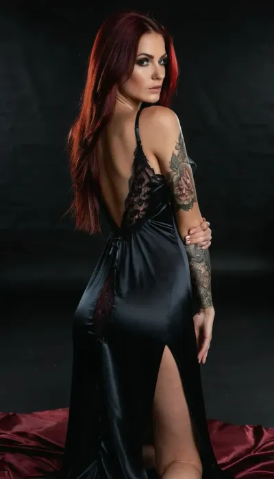 Skinny 25 years woman, long straight dark red hair, Tall, slender woman, black eyebrows, black eye shadow, Absolute darkness around, black background, photostudio, photorealistic, stunning quality, 4k, very large tits, bjg ass, ((black satin nightgown with lace)), (one arm tattooed from shoulder to wrist), languid sexy eyes, slightly turned head, kneeling, ((full clothed, hands pressed ass, hands hold her ass, hands grabbed ass)), head down, looking down