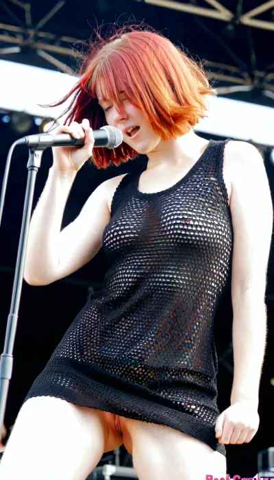 Sexy redhaired, (bobcut), wearing a black coarsely crocheted summer dress, shaking her head, rockband singer pushes her microphone in her pussy on stage during a sunny concert