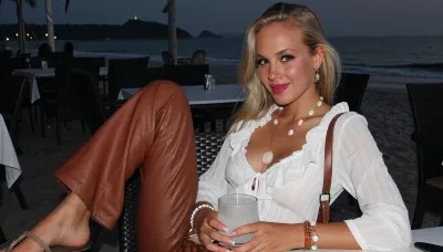 blonde danish girl, 18 years, extreme skinny, tanned skin, ((young face, freckles, intense glossy magenta lipstick, black eyeliner)), flared brown leather pants, white ruffled chiffon blouse, shoulder bag, sandales, sitting in a restaurant, at a beach, in the evening, shell necklace, bracelets, earrings, smiling, ((face, close up)), eating drinking