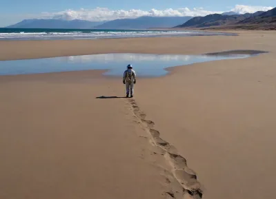 each color is solid and separated from the other by a thin line of a darker shade, bright yellow sand beach with the dunes which contours outlined by dark brown lines in the foreground flows into the soft shapes of the high mountains in the background, their contours outlined by dark grey lines, sky is dark blue, turning into purple in the distance, with red reflections over the mountains, it must be evening, aquamarine of the reservoir complete width of the field of view separates the beach from the mountains on the horizon, lonely small figure of a human in bright silver metal spacesuit with black face shield stands in foreground on the beach, a trail of footprints stretches across the sand from the human to the edge of the image, laconism and graphicity in the drawing of landscape evoke poster in constructivism style and enhance the dramatic effect, is enhanced by the light, which gives almost no shadows, the image is a symbol of loneliness and lostness in space