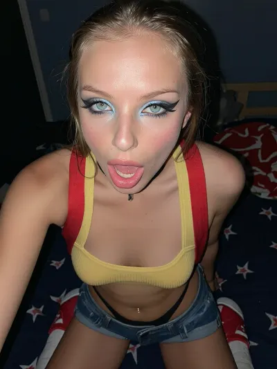 A night-time dark candid hard flash 2010 digital camera shot of a pale-skinned thin 18-year-old ethereal skinny adult Swedish girl, single, bright blue eyes, She is exposing her elegant flat chest, narrow hips, She has an intense facial expression, struggling body, with her lips half parted, an expression of intense dreamy sexual pleasure, eye contact to viewer, She has a lithe thin soft body, (yellow cropped tank top with red suspenders and blue jeans mini-shorts), black thin high-thong, (red sneakers with white ankle socks), dark dorm room, provocative innocent smile, poor lighting, at night, dark, night seductive, saturated glossy pink lipstick, beautiful expressive eyes, seduction, She, She wears elaborate prefectly applied dramatic geometric eye makeup with large bold jagged black winged eyeliner and blue-silver glittery gradients and glossy wet pink lips, blonde side ponytail, (hollow back), wet messy hair, (tanned skin), (supermodel girl), (slim athletic build), (small perky breasts), (big turquoise eyes), black choker, She has a small silver navel piercing, Her vagina is small pink smooth with no hair whatsoever, very dark night time shot with hard camera flash only source of light, specular highlights.