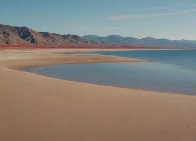 each color is solid and separated from the other by a thin line of a darker shade, bright yellow sand beach with the dunes which contours outlined by dark brown lines in the foreground flows into the soft shapes of the high mountains in the background, their contours outlined by dark grey lines, sky is dark blue, turning into purple in the distance, with red reflections over the mountains, it must be evening, aquamarine of the reservoir complete width of the field of view separates the beach from the mountains on the horizon, laconism and graphicity in the drawing of landscape evoke poster in constructivism style and enhance the dramatic effect, is enhanced by the light, which gives almost no shadows