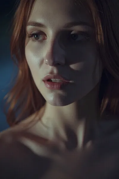 A muted, low-contrast intimate portrait in a very dimly lit, moody night setting with all lights off. The scene is lit only by a very soft, underexposed, diffused ambient light source. The woman's sultry features are defined by subtle, soft-focus shadows. The image has a heavy film grain, and the colors are desaturated and washed out. Her red hair is soft and loose. The overall feel is quiet, intimate, and moody.