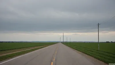 (in Michael Whelan art style), straight narrow old asphalt road stretches away into the distance, along the road are bright green fields and poles with wires on the right, a bright blue sky with white clouds, low mountains on the horizon far away, (saturated bright colors, high definition image, high contrast colors)