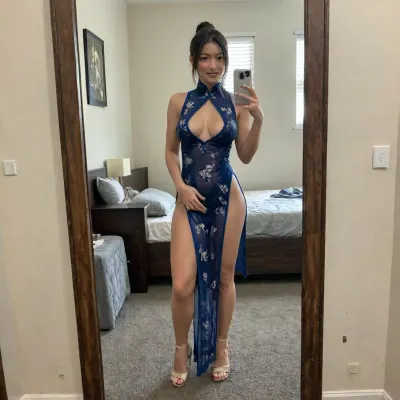 A middle-aged, voluptuous married Japanese woman takes a selfie in a mirror, wearing a qipao, reveals her breasts, shapely long legs, and sexy see-through underwear. She holds a mobile phone in her hands