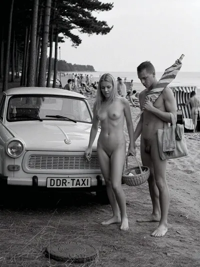 in 1970 on the Baltic Sea coast of the German Democratic Republic, a historically accurate monochrome documentary summer photograph in dramatic East German social realism, high-detail archival black and white photography, a period-correct Trabant parked in the shaded foreground at the edge of a dark coastal pine grove, slightly dusty, plain roof, open passenger door, rectangular front license plate mounted directly on the bumper, clearly reading "DDR-TAXI" in bold uppercase letters, the text integrated like a normal vehicle plate, not a sign, rough sandy ground scattered with pine needles, dry grass, small stones, and tire marks. Beside the car stands an adult young couple, both 25 years old, fully nude in a natural Freikörperkultur context, complete adult nudity shown in a matter-of-fact documentary manner, including his visible penis and her visible breasts, nipples, and pubic area, not erotic and not posed, simply everyday naturist beach life. The woman, long blonde hair, athletic natural figure, calm face, casual posture, locks the Trabant with her right hand using a small key, while a simple wicker beach basket filled with modest food hangs from the crook of her left arm. The man with a relaxed, sporty build carries a folded vintage striped sun umbrella across his shoulders and holds a practical canvas bag with towels, he has a penis, Both move naturally, caught mid-action. Behind them, the pines open toward a busy Baltic naturist beach with many clearly adult vacationers, men and women of different adult ages, all naturally nude, walking, sitting, talking, sunbathing, arranging towels in a casual, respectful atmosphere, several traditional hooded wicker beach chairs with striped fabric and curved canopies, vintage windbreaks, canvas bags, thermos flasks, enamel cups, folded newspapers, soft dunes, pale sand and the calm Baltic Sea. Strong tonal contrast, realistic analog film grain, high texture detail, deep shadows and bright haze, candid composition, respectful historical documentary style, no modern objects, no erotic posing, only authentic 1970s DDR summer life.