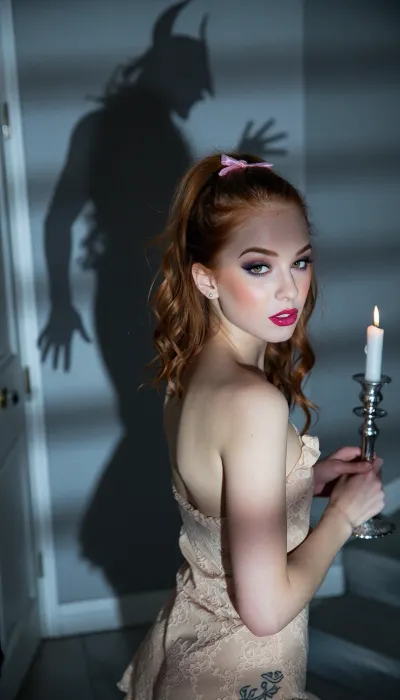 A hyper-detailed realistic photograph. A small natural bust and a lean frame, porcelain skin, with a faint flush, in her late twenties, red hair, in loose curls, full, wide lips, large doe eyes, a lit-from-within bronzy glow with golden highlighter on the cheekbones and a satin nude lip, an ornamental blackwork tattoo on her lower back, the ink sitting on her natural skin, matching small silver studs in her earlobes.This cinematic portrait captures a attractive petite girl with glossy magenta lips and pastel eyeshadow, blurring the foreground into soft out of focus, The color grade is cold blue-silver and desaturated, misty atmosphere around her body, glow specular highlights, bokeh background, strong prismatic color separation on speculars, bold feline eyeliner, dark red lips, dark grey and silver eyeshadow, golden-amber eyes that create a powerful gaze, high detail, very aesthetic. The scene depicts a horrific scene of a a sinister shadow descending on a wall behind a female. The female wears a short lace night dress. Her dark blonde hair is up and tied with a pink ribbon. The short nighty is sleeveless but loose around her body. She holds a silver candlestick holder with a lit candle that provides dim light to the dark and horrific scene. She is walking up a staircase and is seen in a side view as she begins to turn her head to look behind her, ((She senses a presence that is not seen in the frame, but a creepy whitch shadow of a horrific being is seen on the wall behind her. The shadow has hunched posture as though it is cast by an old being. The shadow's outstretched fingers are about to descend on the female. The mood is creepy and foreboding)), fierce hypnotic expression, Deep black background, ultra high quality, subtle atmospheric haze, high contrast chiaroscuro, shimmering metallic reflections, mysterious dark fantasy aesthetic, ultra-detailed textures, cinematic photography, 85mm lens, photorealistic, high fashion editorial, (9:16), vertical composition, The image uses a wide shot showing her full body, a low angle from her side, the camera near her hip line and a wobbling handheld framing. Her skin shows natural texture including visible pores, slight sheen from candelight, and subtle shadows cast across her torso by the overhead fabric. The background is washed out in dark candlelight, suggesting an indoor setting under dim lit, contributing to a candid, raw digicam aesthetic with high contrast between highlights on her skin and deep shadows beneath her body.The final treatment uses blown highlights and an orange light leak on one frame edge and washed faded colour.