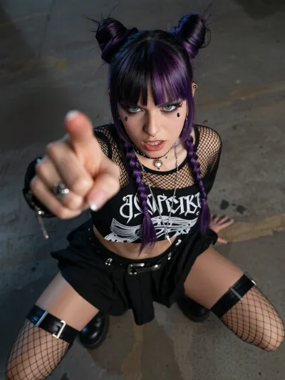 A gorgeous 19yo punk model with dual-toned black and purple hair squatting on a concrete floor, punching directly into the camera, flashing pussy, heavy punk makeup, necklaces, earings, nose stud, navel piercing, wearing a fishnet top over a band tshirt and a short pleated skirt, knee high boots, twin-bun hairstyle, long braids, fishnet stockings, garter belt, angry expression