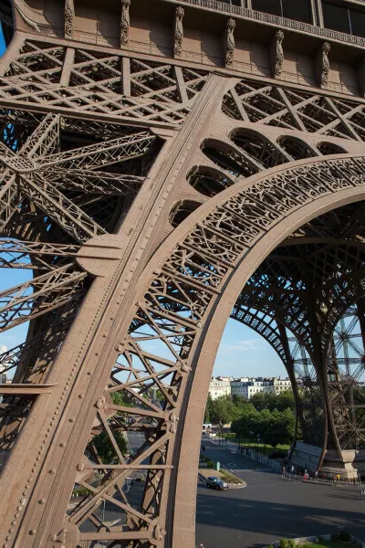 An ultra-detailed architectural photograph of a detailed section of the Eiffel Tower, featuring a hyper-realistic texture of the iron latticework, of the highest commercial quality, sharp focus on intricate metal elements and rivets, bright morning sunlight casting sharp shadows, stunning depth of field with the streets of Paris visible in the distance, a photorealistic masterpiece, award-winning photograph, cinematic lighting.