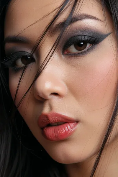 intimate portrait of a Chinese woman with heavy kohl eyeshadow and thick winged eyeliner, 60s aesthetic of a noir dame, loose strands of hair falling into her eyes and tangling in her long eyelashes, luscious soft lips painted in a vivid red with wrinkled pillowy creases