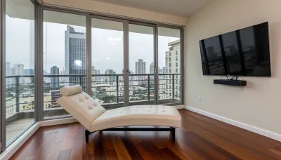 The scene is a high-rise apartment, skyscraper, large floor to ceiling windows, aged mahogany floors, a cream colored leather chaise lounge, a large Golden pathos, 75 inch TV on the wall, a balcony.