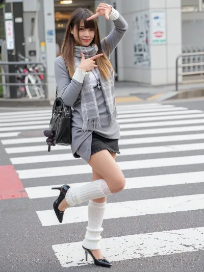 High angle full body shot of a beauty Japanese female model of Shibuya style standing on a pedestrian crossing. She is making a "hand frame" gesture towards the camera with a playful smile.She is in leg-lengthening pose, one foot extended towards the camera, pointed toes. 1girl, solo, asian woman, Japanese idol face, smooth and fair skin, long ombre brown hair, Straight hair, Bangs, curvy, perfect female body, slender legs, toned legs with curves, gigantic breasts. Her outfit consists of a gray, fitted, long sleeves dress.The Innerwear is a white top with white trim extended sleeves at the neckline and cuffs.Underneath the dress, a washed black denim short skirt is visible.She carries a black leather shoulde bag with a cute bear charms over her shoulder.White thighhighs with lace, Whiteslouchy knit leg warmers pulled up to just below the knees, loose and stacked around the calves, not tight, not skin-tight.black leather stiletto high heels with pointed-toe.gray plaid oversized scarf and cross necklace. The background is a Shibuya urban street with zebra crossing markings, soft bokeh effect.natural daylight, She has messy hair glowing in the backlight.Serene expression, basking in the warm afternoon sun. High key lighting, airy atmosphere, overexposed aesthetic, soft pastel tones, cinematic film grain, minimalist urban background with red road markings. instagram story style, vertical smartphone video frame, casual selfie vibe, slightly overexposed highlights, soft blown highlights from street lights, subtle lens flare, low bitrate compression, social media noise, slight gaussian blur, motion from hand holding phone, unsteady framing, imperfect autofocus, authentic phone camera look.
