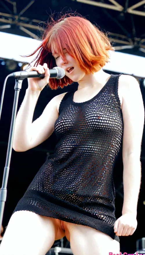 Sexy redhaired, (bobcut), wearing a black coarsely crocheted summer dress, shaking her head, rockband singer pushes her microphone in her pussy on stage during a sunny concert