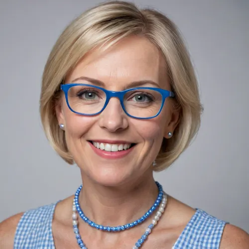 Close-up portrait of a smiling middle-aged woman with short blonde hair, wearing square glasses with blue frames, a light blue and white gingham dress, and a statement necklace of blue and white circular beads. The background is plain white. Natural lighting, head-and-shoulders shot, realistic style, high detail.
