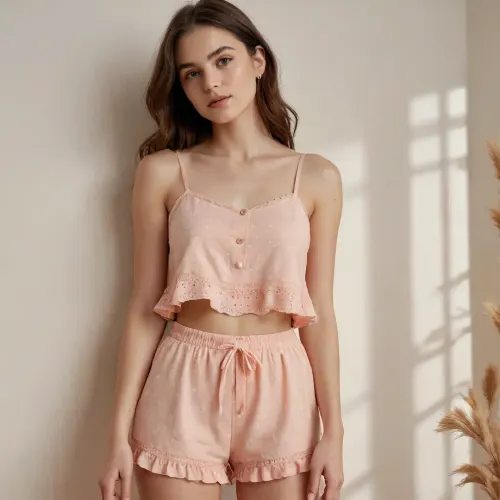 The outfit is a two-piece loungewear set in a soft peach or light coral color. The fabric appears to be a lightweight material, possibly cotton or a blend, with a delicate floral print. The print consists of tiny white flowers scattered across the peach background. The texture of the fabric seems to have a slight raised quality, perhaps due to embroidery or a textured weave, evident in the eyelet-like details around the edges.

The top is a cropped camisole with thin straps. It has a relaxed, flared silhouette that ends just above the navel, creating a playful and airy feel. The hem of the top is finished with a ruffled edge, adding a touch of femininity. The neckline is simple and straight, and the straps are thin and adjustable.

The bottom is a pair of high-waisted shorts. They fit snugly around the hips and are also cropped, revealing a bit of the midriff. Similar to the top, the shorts feature a ruffled hemline, creating a cohesive and charming look. The eyelet detailing is also present along the edges of the shorts.

The overall style aesthetic is casual, feminine, and slightly bohemian or vintage-inspired, reminiscent of delicate sleepwear or summer loungewear. The color palette is soft and summery, and the floral print adds a touch of sweetness. The relaxed fit and ruffled details contribute to a comfortable yet stylish appearance, suitable for lounging at home or for a casual warm-weather occasion.

Bedroom
