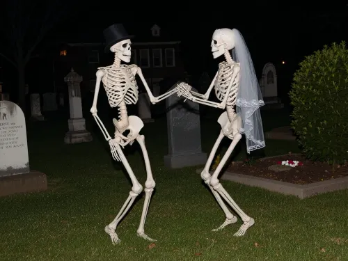 two skeletons are dancing side by side on a graveyard at night, one had a top hat on, the other has a brides vail on