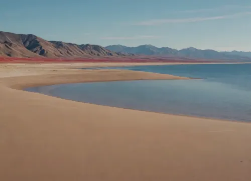 each color is solid and separated from the other by a thin line of a darker shade, bright yellow sand beach with the dunes which contours outlined by dark brown lines in the foreground flows into the soft shapes of the high mountains in the background, their contours outlined by dark grey lines, sky is dark blue, turning into purple in the distance, with red reflections over the mountains, it must be evening, aquamarine of the reservoir complete width of the field of view separates the beach from the mountains on the horizon, laconism and graphicity in the drawing of landscape evoke poster in constructivism style and enhance the dramatic effect, is enhanced by the light, which gives almost no shadows