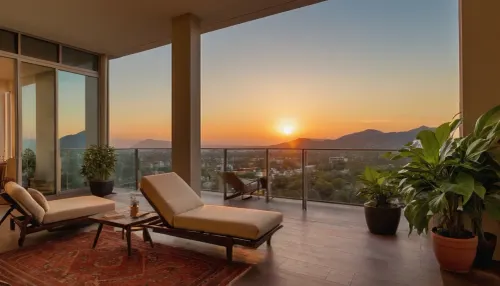 The scene, looking out at the sunset on the corner balcony of a 12 ft ceiling apartment, large floor to ceiling windows, skyscraper, stone floors on the outside, mahogany wood floors on the inside, inside is an open floor style floorplan, a cream colored lounge chair is on the inside, a burnt-ornange deck chair is on the outside. SEVERAL PLANTS are on the inside and outside of the apartment, [types of plants include a matured mix of the following], (Epipremnum aureum), (Dracaena trifasciata), (Philodendron scandens), (Hedera helix), far in the distance is a mountain that is deeply forested, one of the plants hangs from the ceiling. The balcony is half ceiling half skylight.