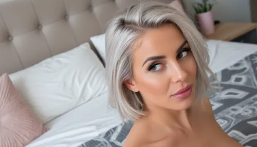 intimate portrait of a sultry woman posing sensually in her cozy bedroom with minimalist feminine decor, huge expressive eyes looking away in a coyly suggestive side-eye glance, her voluminous silvery-blonde hair in a cut in a short bob with one side swept back in a tousled finger combed look, her soft glossy lips are quirked in a smug smirk, delicate triangular face with high chiselled cheekbones, high-angle shot as she sits on her bed, the subject is anchored to the side image with her bed featured prominently in the background using a rule-of-thirds composition